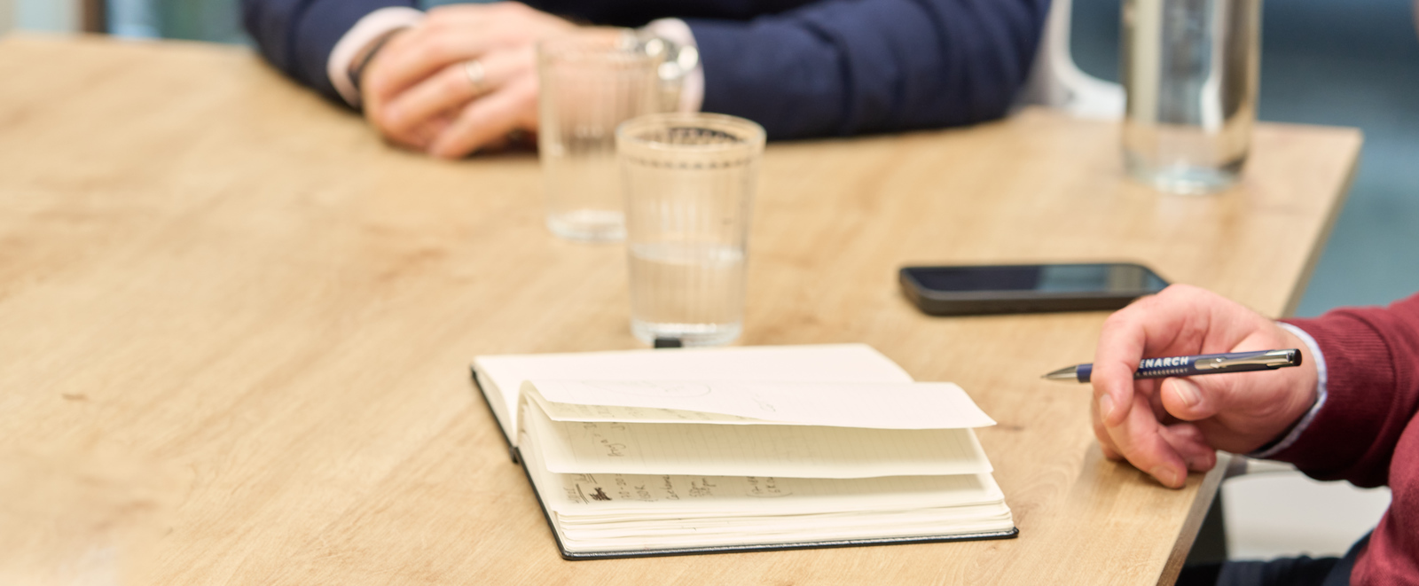 Close-up of a meeting table with a notebook, pen, glass of water, and smartphone